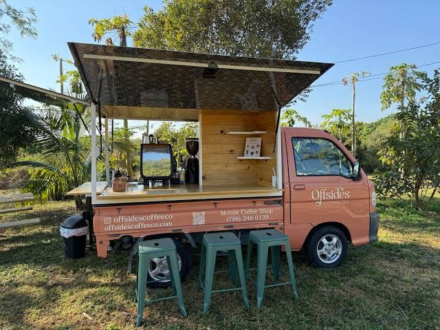 A compact pink coffee shop on wheels with its canopy open and stools nearby